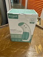 Photo of the Arespark CS11 Portable Garment Steamer in its original box on a wooden table.