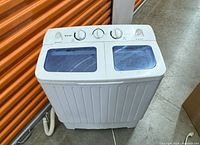 Front angle of white twin tub portable washer and spin dryer unit showing control knobs and lids with transparent windows.