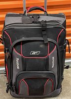 Front view of the black and red Reebok suitcase showing multiple zippered compartments and the retractable handle.