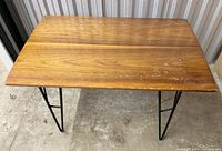 Wooden side table with metal hairpin legs from a top-down angle, showing wood grain and surface wear.
