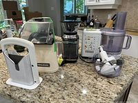 Overview of all four appliances on kitchen counter: bagel cutter, popcorn maker, coffee grinder, food processor with attachments.