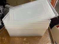 Stack of eight clear rectangular plastic storage containers with lids placed on a wooden surface.