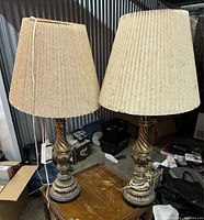 Pair of ornate table lamps with fabric shades in a storage setting showing need for cleaning.