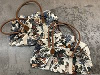 Photo of two matching travel bags with floral pattern and brown handles on concrete floor.