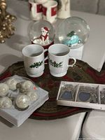 Photo showing the full lot including two musical snow globes, two holiday mugs with holly and cranberry designs, set of white/silver ornaments, two metal decorative frames, and the Florentine-style tray.