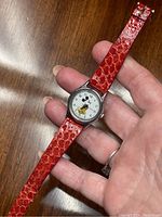 Full view of the vintage Mickey Mouse watch with red snakeskin patterned strap held in hand showing overall condition and design.