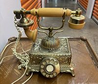 Front view showing the rotary dial, ornate metal base, and cream handset with brass accents.