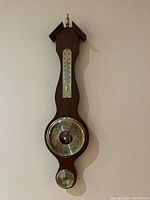 Photo of wooden wall-mounted weather station showing barometer, thermometer, and hygrometer dials.