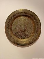 Photo showing a round brass plate with intricate floral and geometric engravings covering the surface and rim.