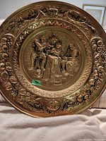 Close-up of round brass plate with detailed relief of people and decorative border