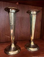Pair of tall brass candlesticks with etched details and weighted bases on a wooden surface.