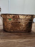 Hammered copper tub with textured surface, flat base, and reinforced top rim, placed on wooden floor.