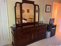 Dark wood dresser with nine drawers and two cabinet doors, topped with a three-part mirror. Brass-tone hardware on drawers and doors. Mirror panels have curved top edges. The dresser appears in good condition with polished finish.