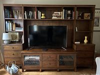 Front view of three piece Ethan Allan entertainment unit with TV on stand, shelves with books, and various decorative items.