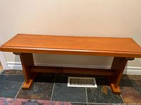 Photo showing a wooden hall bench with rectangular top and solid support legs placed on a tiled floor.