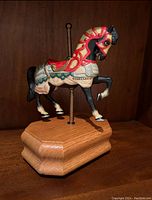 Photo of a carousel horse music box on a wooden base with a brass pole, showing the painted decorative horse figure.