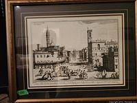 Framed black and white print showing a busy historical European cityscape with clock towers and people in period clothing.