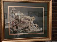 Framed print showing a muscular nude man using a compass on a scroll, framed with gold-tone frame and double matting.