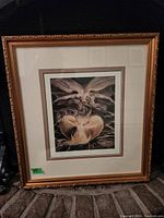 Photo of framed print showing mythical or fantasy winged figures with detailed gold frame and double matting.