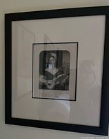 Framed black and white print showing a woman with a guitar, housed in a black frame with white matting.