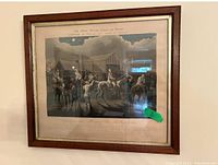 Framed print depicting "The First Steeplechase on Record" with horses and riders in a rural setting with text below the image. Wooden frame and glass protection visible.