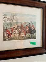 Framed antique print showing a fox hunting scene with riders on horses in red hunting jackets at a fence.