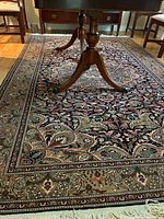 Close-up of rug showing central navy field with floral vine pattern, cream border and fringe edge.