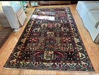 Photo of a multicolored rectangular area rug with intricate geometric and floral motifs placed on a hardwood floor between cream-colored furniture.