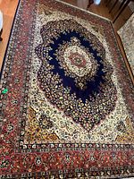 Overhead view of rectangular Persian-style rug with central medallion and floral border in navy, ivory, red, and gold on hardwood floor
