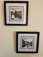 Two framed Asian style black and white prints, each showing water canal scenes with East Asian characters in the top left corner, mounted on a beige wall.