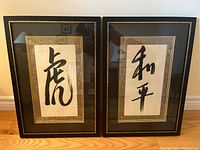 Front view of two framed Asian calligraphy prints hung side by side on a wall.