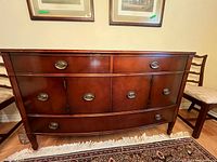 Frontal view of dark wooden sideboard with brass oval handles, two small top drawers, two cabinet doors, and two lower drawers.