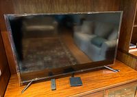 Front view of Sony TV on wooden surface with remote control and connected device box