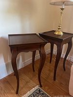 Two small wooden side tables placed next to each other on a wooden floor with a brass lamp on one table.