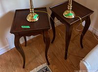 Photo of two wooden side tables with square tray tops and curved legs placed on hardwood floor near a wall and sofa.