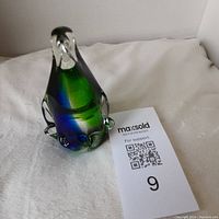 Art glass penguin, clear glass body with blue and green colors inside, shown on white cloth background with MaxSold card