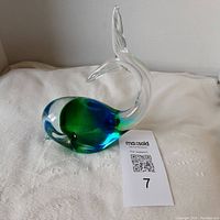 Blue and green Murano style art glass whale figurine on a white cloth background with auction tag.