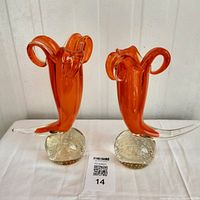 Pair of bright orange cornucopia vases on clear bubble bases shown side-by-side on table.