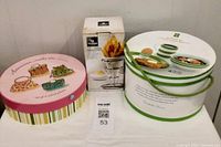 Photo of three boxes containing the assortment of plates and kitchen serving items, showing round boxes and a package containing a metal stand with small bowls.