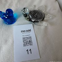 Blue bird and art glass turtle figurines on white fabric background with MaxSold auction card