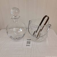 Glass cognac decanter and crystal ice bucket with tongs shown side by side.