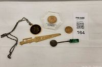 Photo showing the metal necklace with round '3' pendant, several coins including one in a protective case, a wooden carved stick with Asian characters, and a small wrapped item attached to a stick.