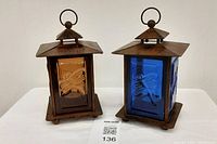Two bronze-colored lanterns with colored glass panels showing dragonfly embossing, viewed from the front.