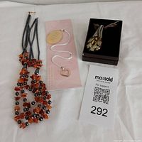 Lot of three jewelry items including orange and black bead necklace, Murano style glass pendant necklace in box, and heart charm bookmark with white cord.