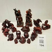 Full view of the deep red resin collection showing all figurines including Buddhas, monks, horses, elephants and a duck on a white surface.