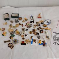 Overview of assorted pins laid out on white cloth including some small boxes