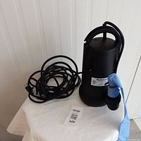 Full photo of the submersible pump with attached blue tubing coiled next to it.