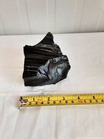 Photo showing a large piece of shiny black obsidian rock measured against a tape measure placed horizontally, showing about 4 inches in width.