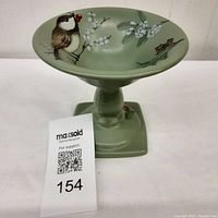Front view of a green ceramic candy dish with a bird and white berries painted inside the shallow bowl, shown with lot number tag.