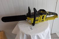 Full view of Ryobi chainsaw with blade cover, placed on white cloth